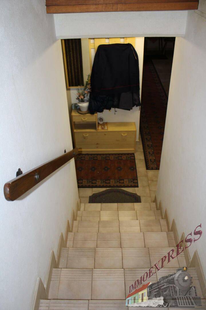 Treppenabgang in den Keller mit gefliesten Stufen und Holzgeländer.