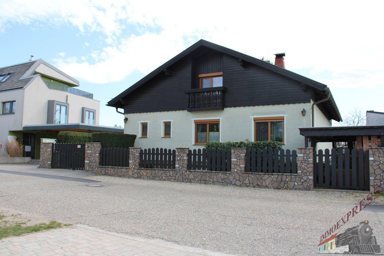 Gesamtansicht des Hauses von der Straße mit Zaun und angrenzendem Nachbargebäude.