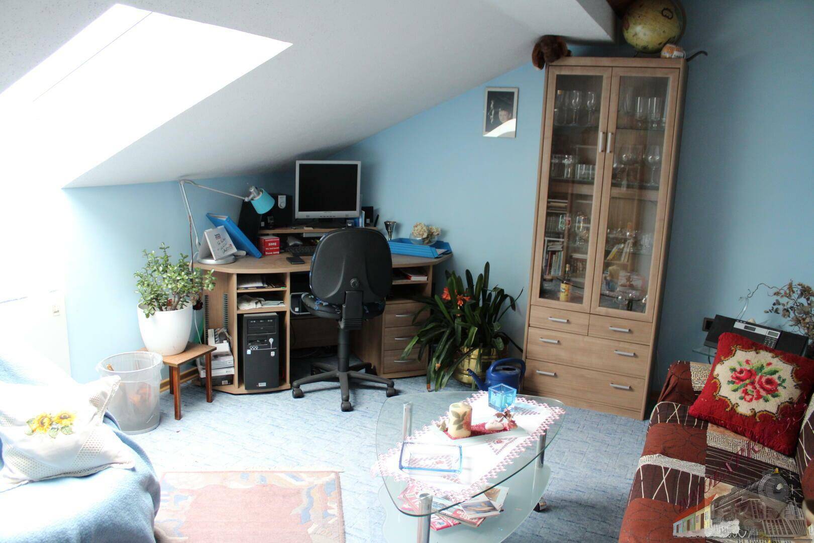 Helles Arbeitszimmer im Dachgeschoss mit Schreibtisch, Schrank und Dachfenster.