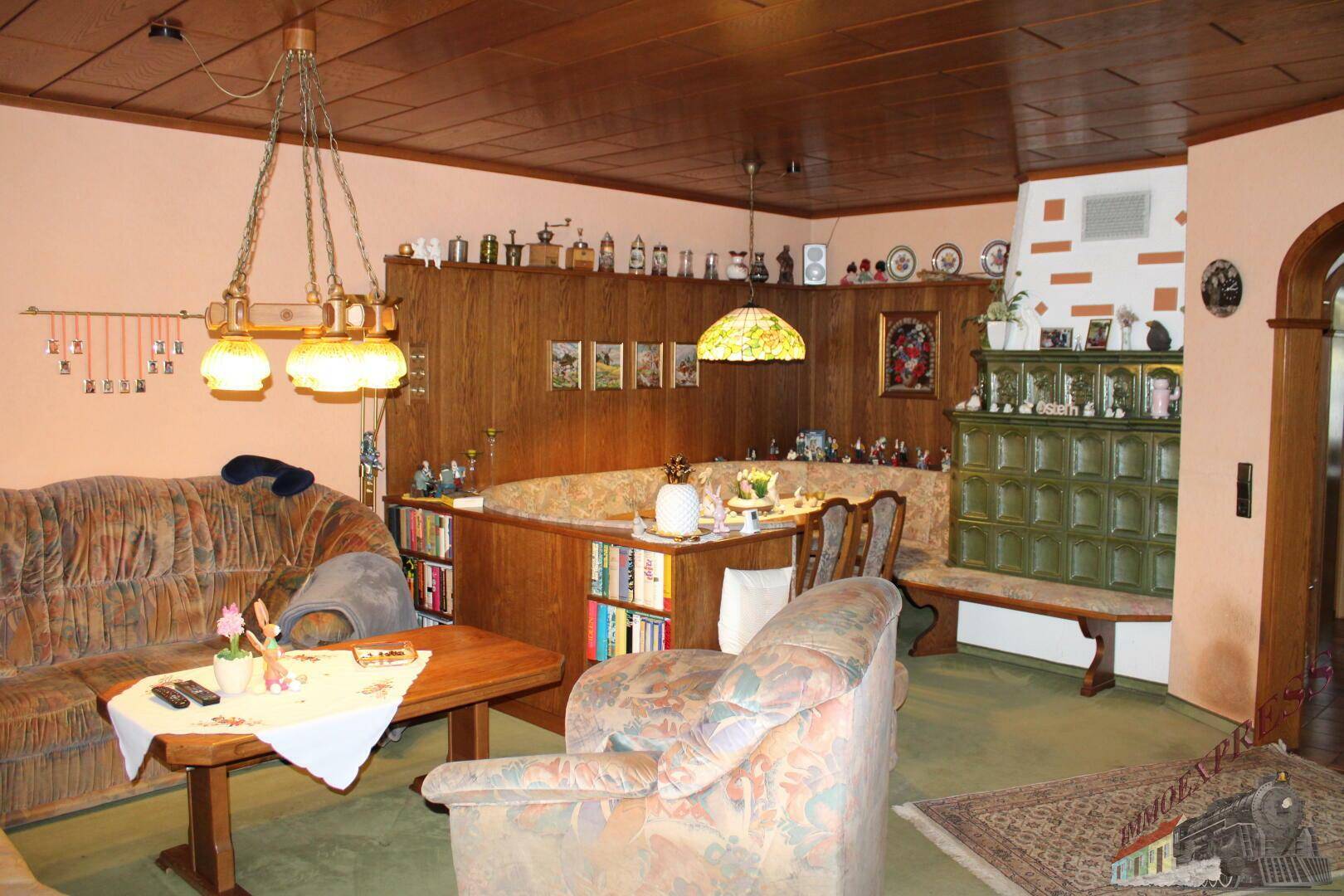 Traditionelles Wohnzimmer mit Kachelofen, Holzdecke und gemütlichen Sitzmöbeln.