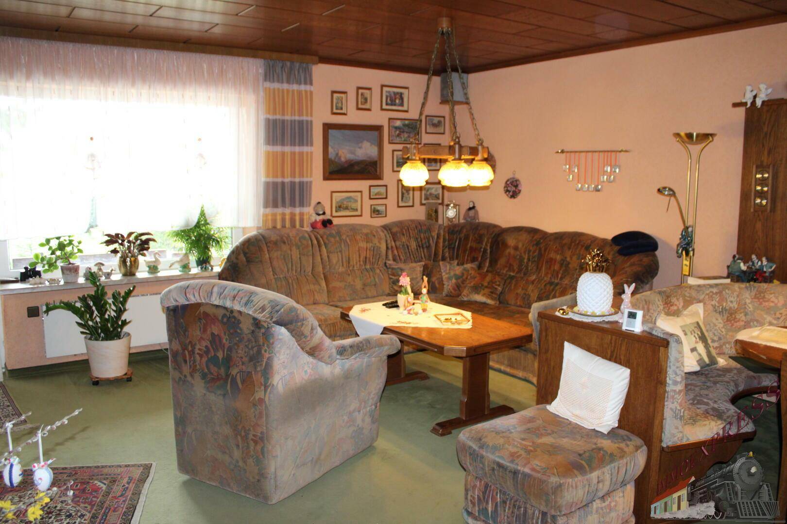 Gemütliches Wohnzimmer mit großem Ecksofa, Teppichboden und vielen persönlichen Dekorationen.