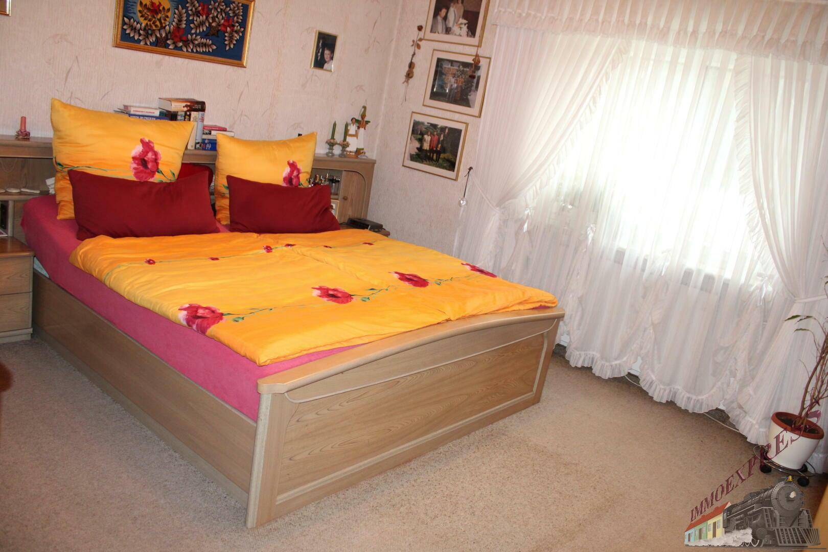 Helles Schlafzimmer mit Doppelbett, Teppichboden und großem Fenster.