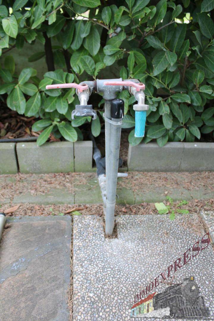 Außenwasserhahn im Gartenbereich, umgeben von Grünpflanzen.