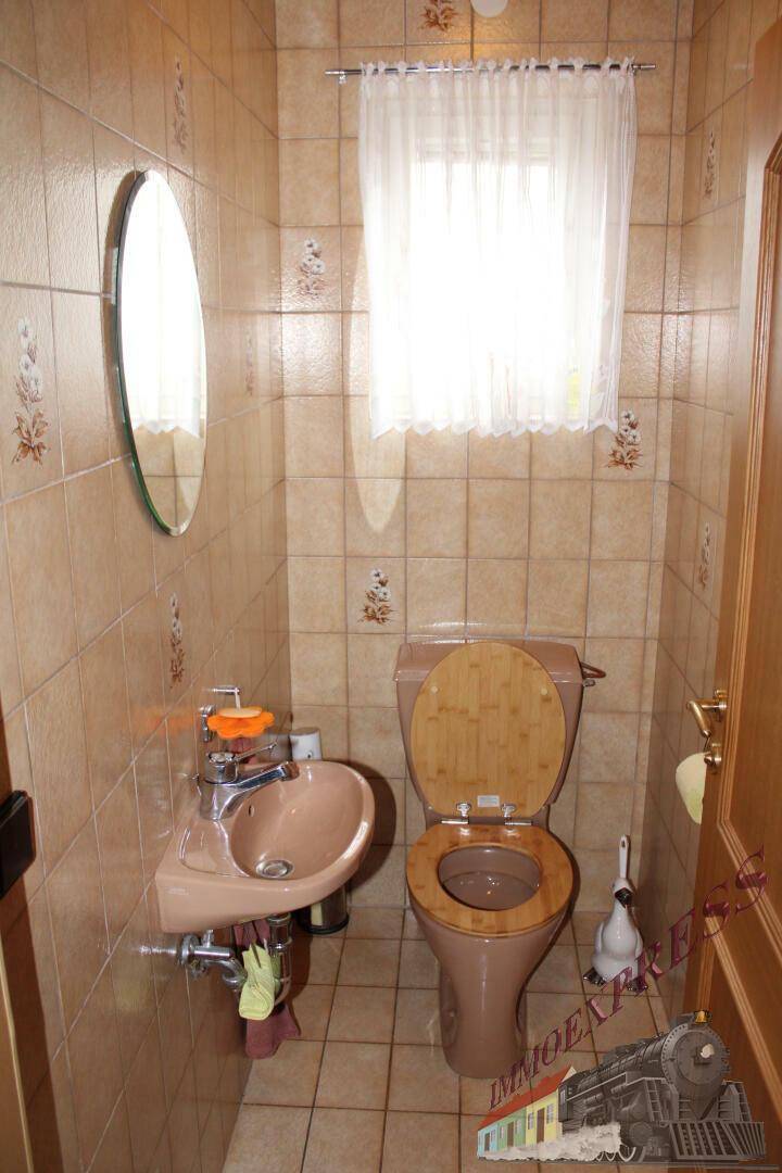 Kleines Gäste-WC mit Fenster, Toilette und Waschbecken in beigen Farbtönen.