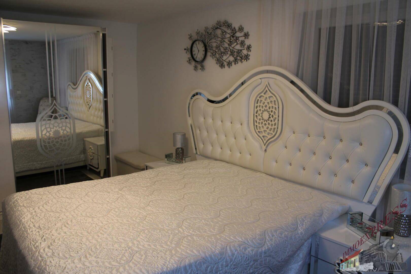 Elegantes Schlafzimmer mit weißem, gepolstertem Bett und Spiegelschränken.