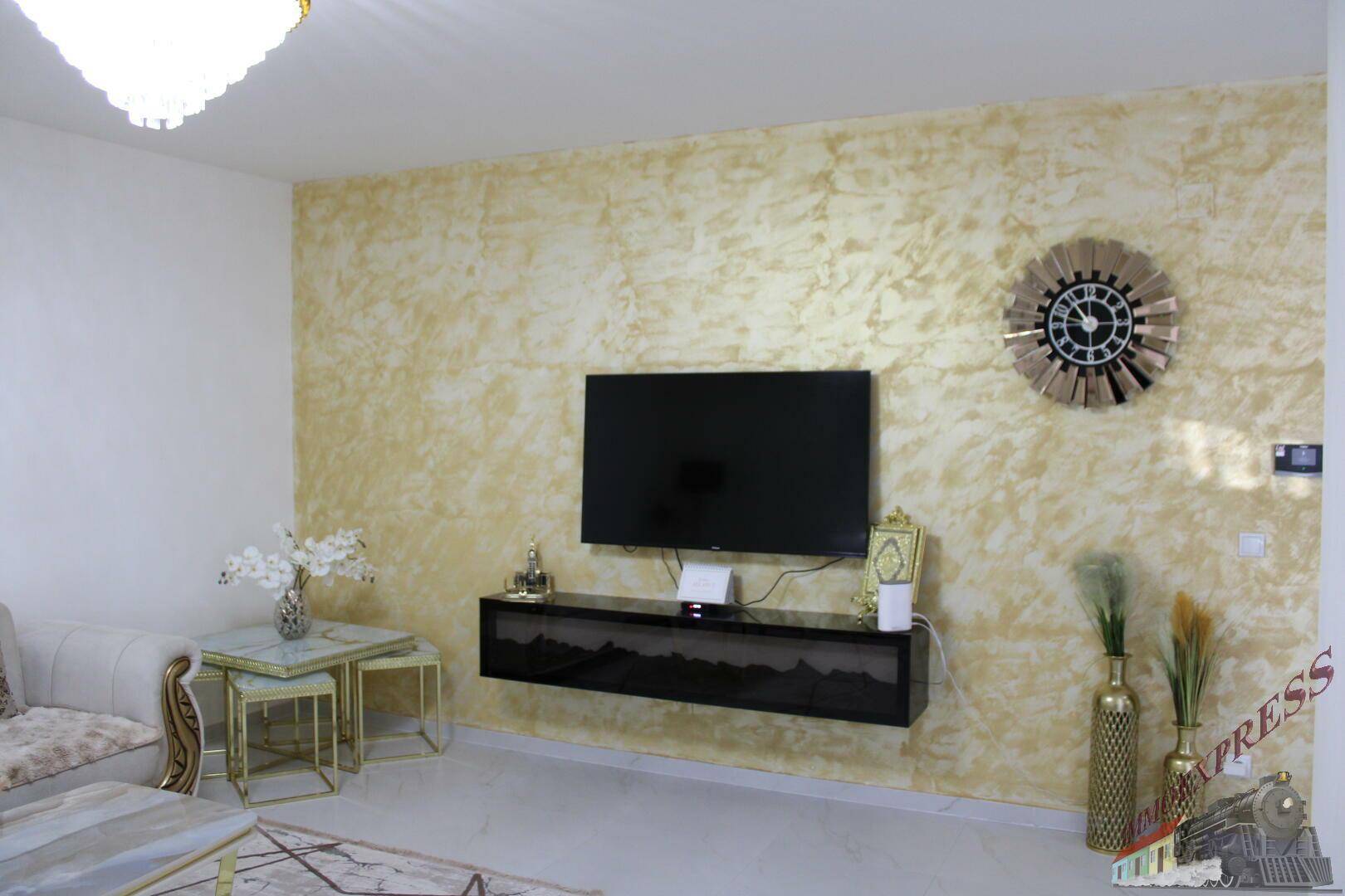 Wohnzimmer mit dekorativer Wandgestaltung, wandmontiertem Fernseher und stilvoller Uhr.