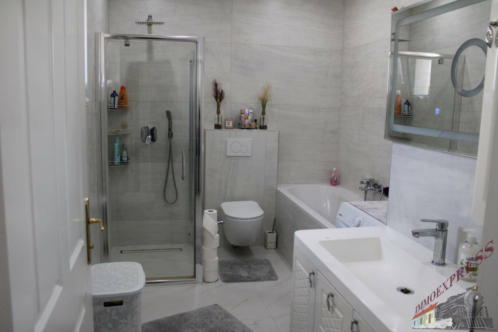 Modernes Badezimmer mit Badewanne, Dusche, Einzelwaschbecken und hellen Fliesen.