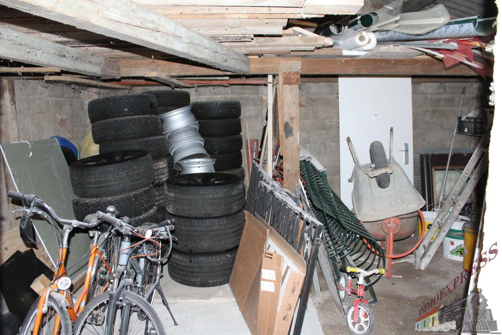 Unaufgeräumter Kellerraum mit Reifenstapeln, Fahrrädern und verschiedenen Lagergegenständen.
