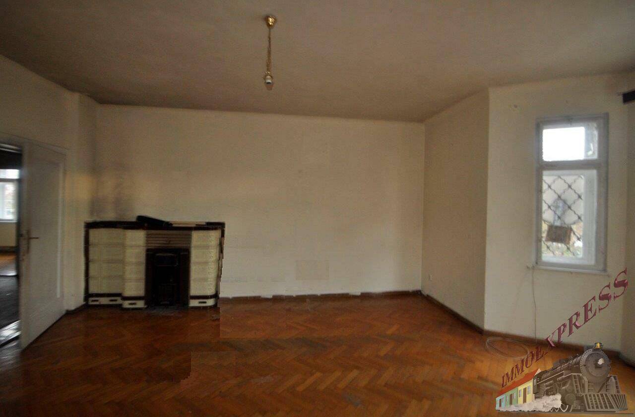Heller Wohnbereich mit Fischgrätparkett, einem Fenster und einem traditionellen Ofen an der Wand.