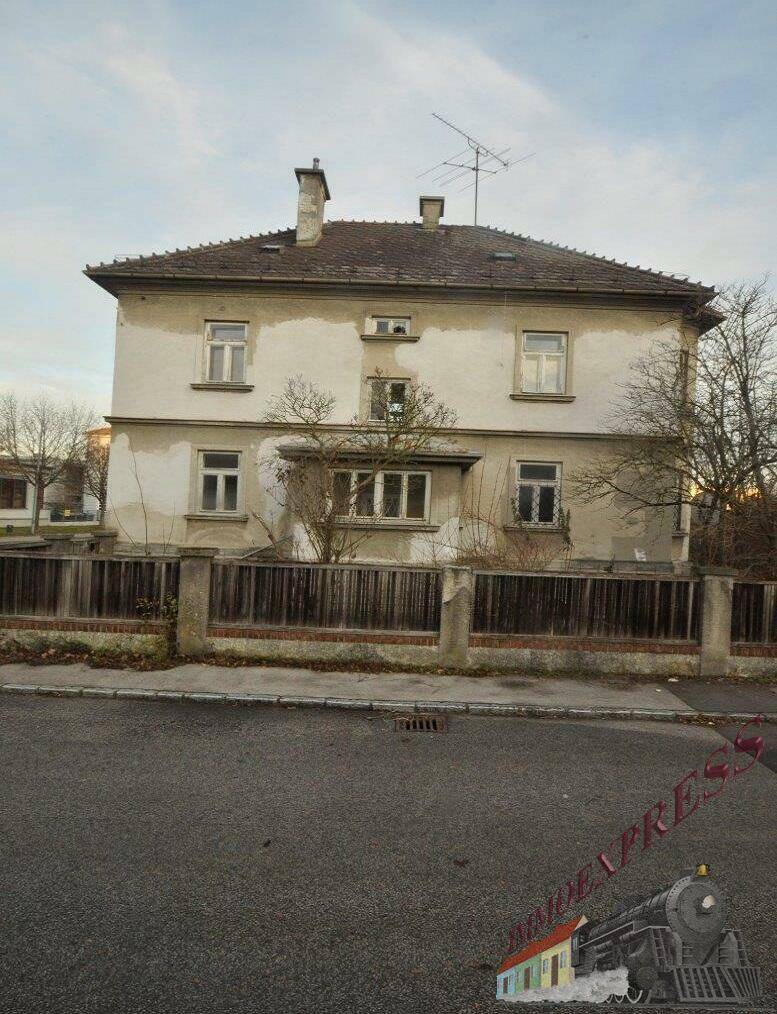 Älteres Wohnhaus mit Putzfassade und mehreren Fenstern, von der Straße aus gesehen.