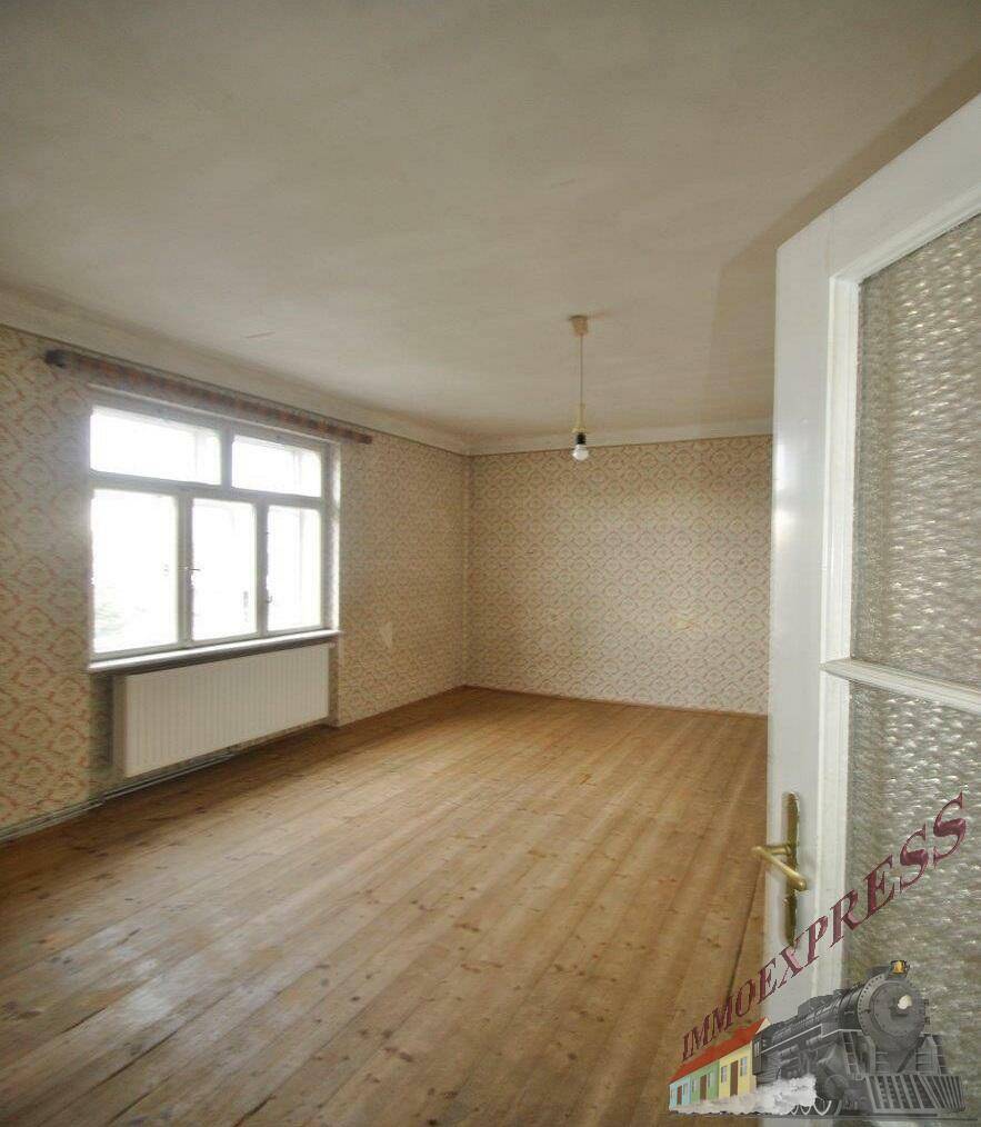 Schlafzimmer mit gemusterter Tapete, Holzdielenboden und einem großen Fenster, das viel Licht hereinlässt.