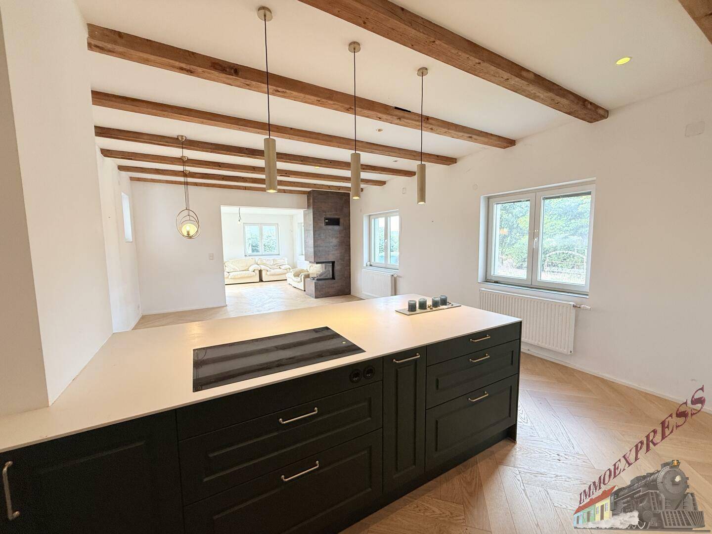 Blick von der modernen Küche in den Wohnbereich, mit Fischgrätparkett, Holzbalken und viel Tageslicht.