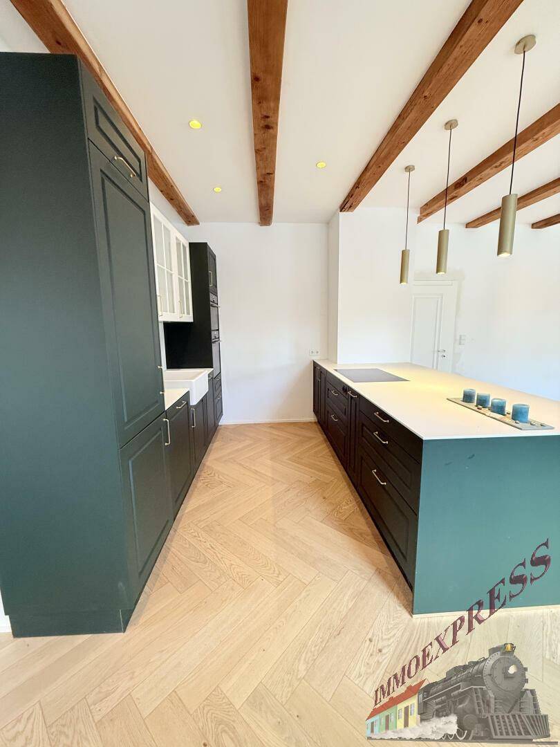 Geräumige moderne Küche mit dunklen Schränken, weißer Arbeitsplatte und Fischgrätparkett, unter Holzbalken.