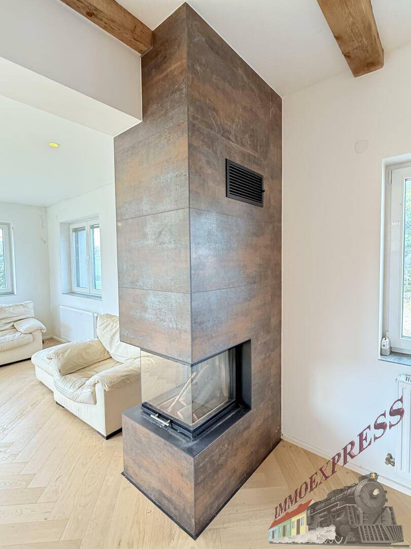 Moderner Kamin mit Holzverkleidung und Glasfront, zentral im Wohnbereich platziert, auf Fischgrätparkett.