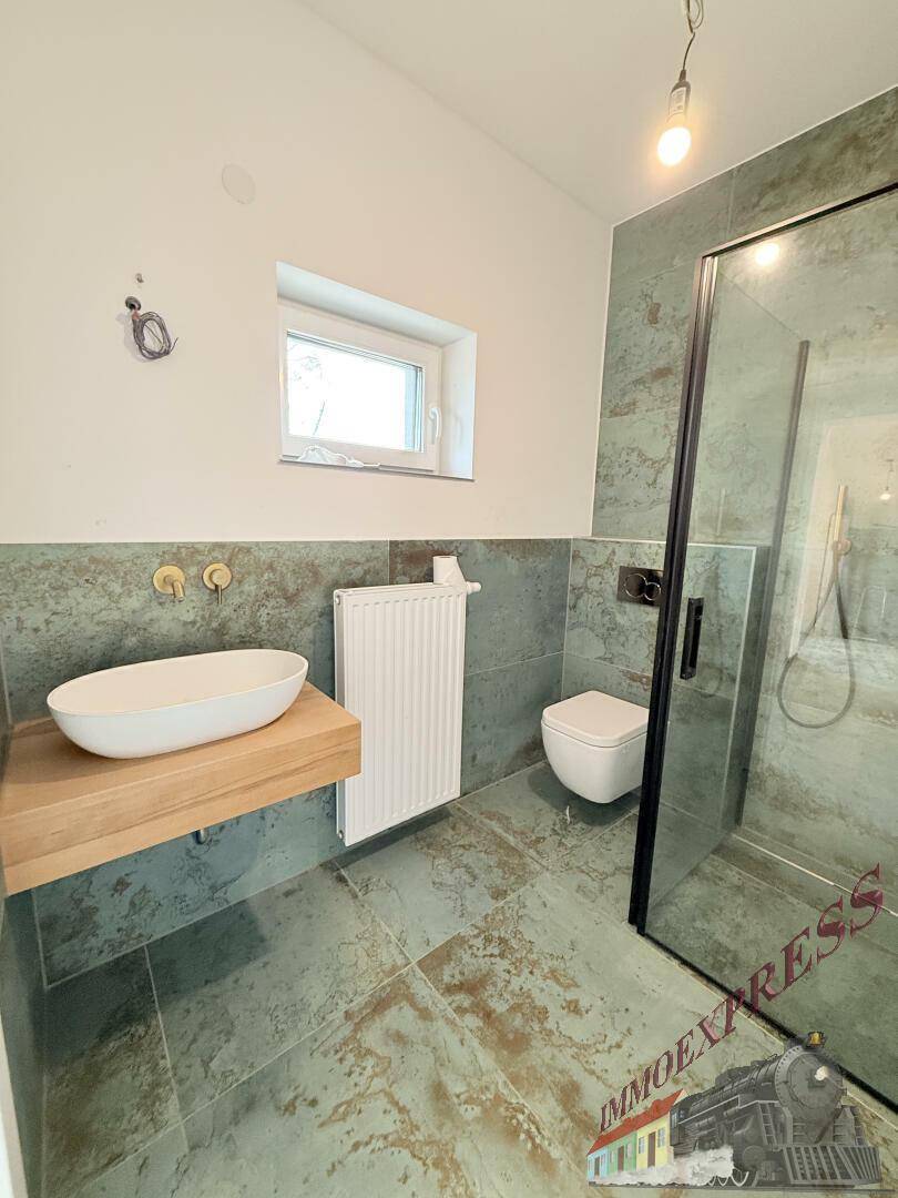 Helles Badezimmer mit modernem Waschtisch, wandhängendem WC und großer Duschkabine mit Glaswand.