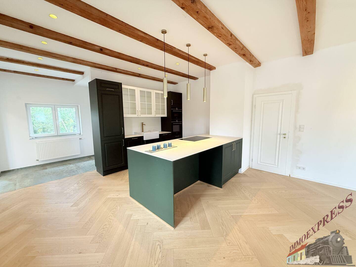 Moderne Küche mit dunklen Schränken, Kücheninsel und Fischgrätparkett, unter sichtbaren Holzbalken.