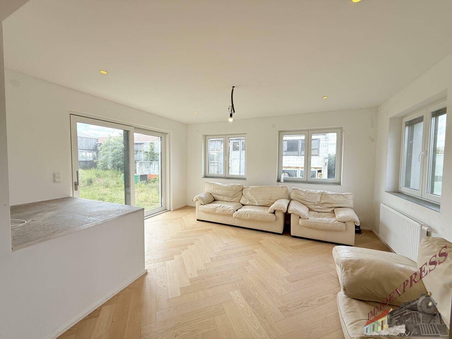 Helles Wohnzimmer mit großen Fenstern, Fischgrätparkett und bequemen Sofas, mit Zugang zum Außenbereich.