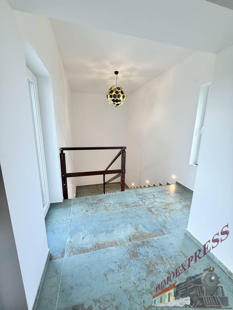 Heller Treppenaufgang mit Fliesenboden und Holzgeländer, führt zu den oberen Etagen des Hauses.