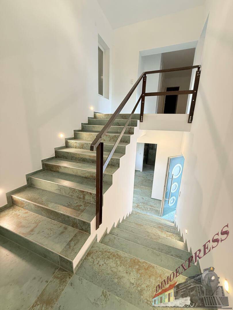 Moderne Treppe mit Fliesenstufen und Holzgeländer, beleuchtet durch integrierte Wandleuchten.