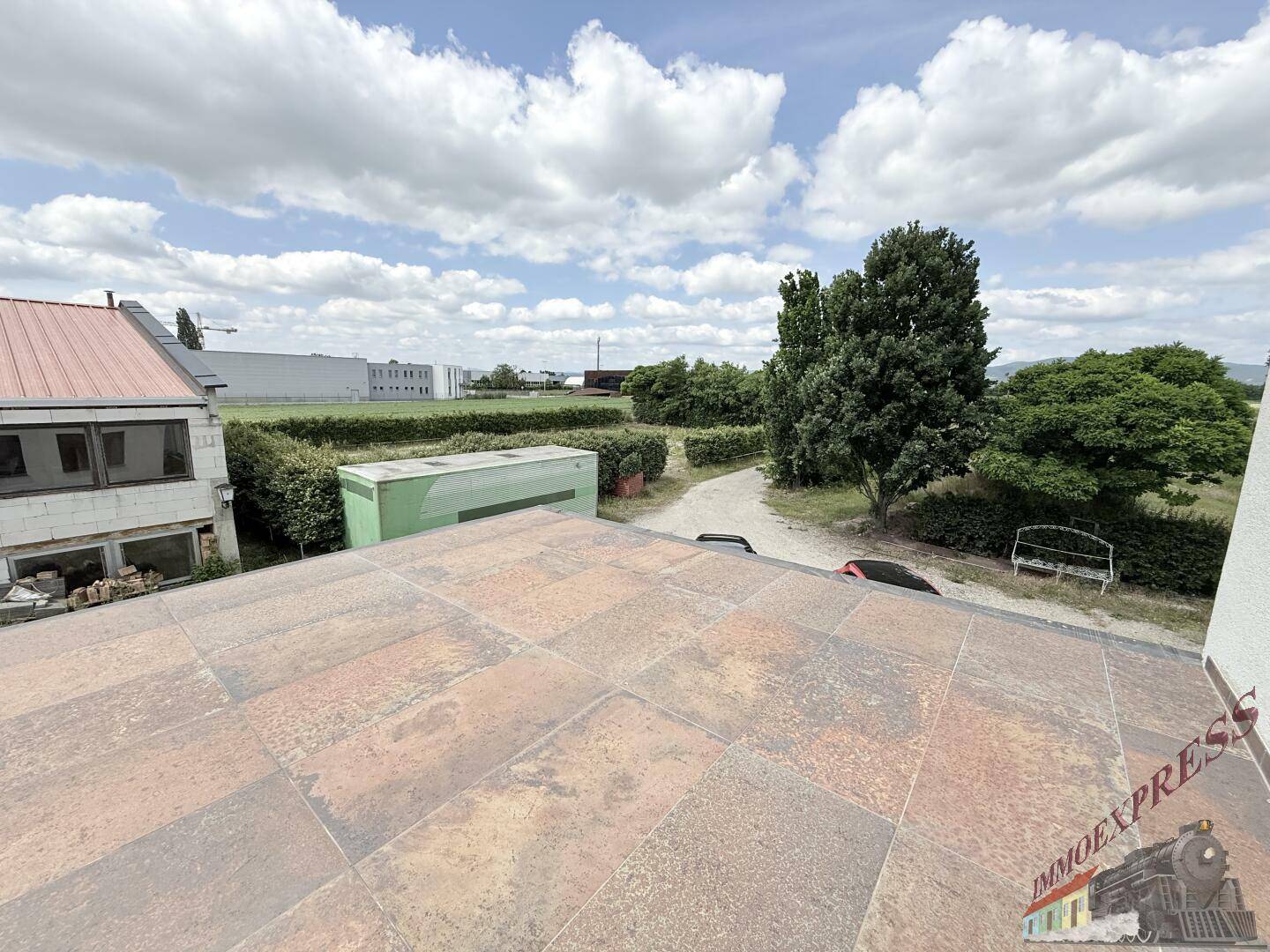 Große Dachterrasse mit robusten Fliesen und Blick auf die grüne Umgebung und weitere Gebäude.