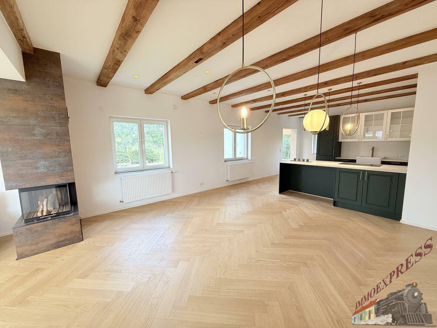 Offener Wohn- und Küchenbereich mit sichtbaren Holzbalken, Fischgrätparkett und moderner Kücheninsel.