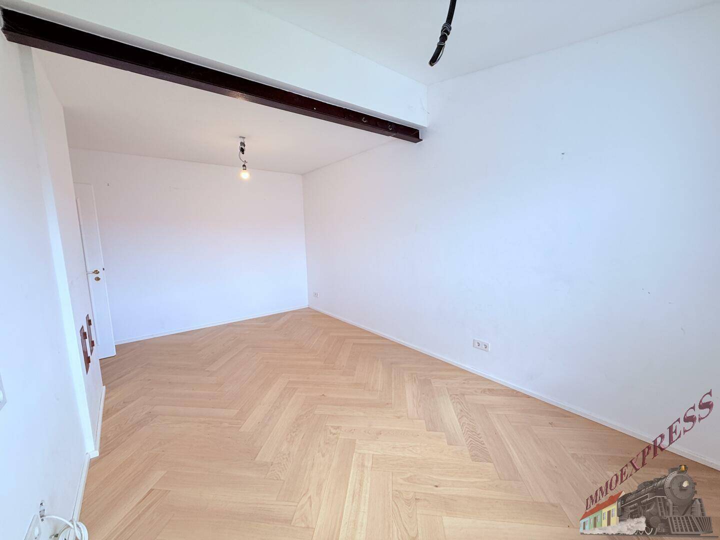 Leerer Raum mit Fischgrätparkett und weißen Wänden, bereit für individuelle Gestaltung.