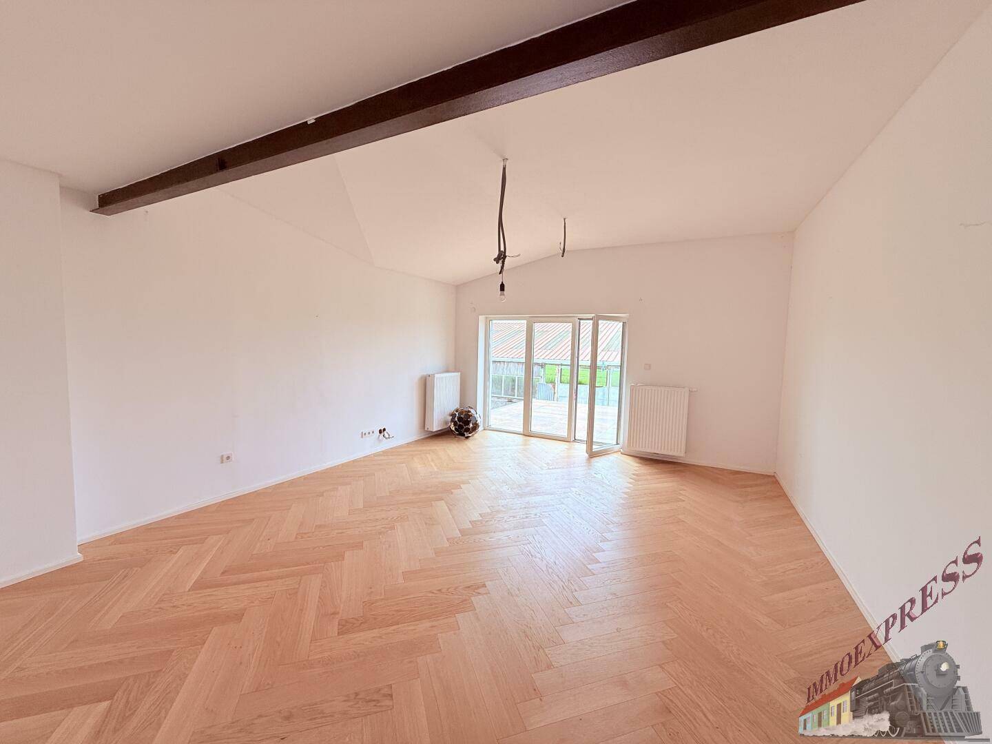 Geräumiger Raum mit Fischgrätparkett und Zugang zu einem Außenbereich durch eine große Schiebetür.