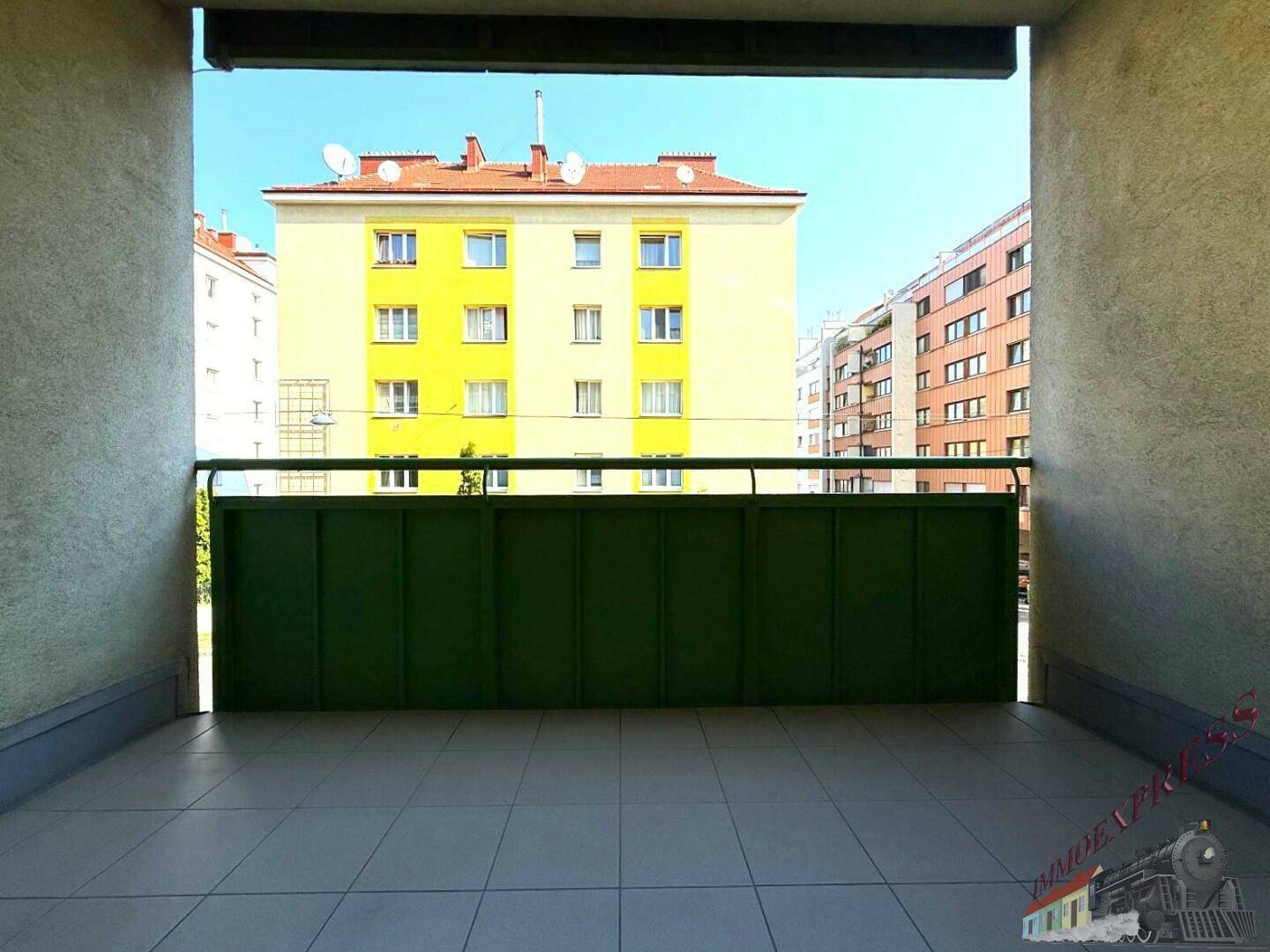 Überdachte Loggia mit Fliesenboden und Blick auf die gegenüberliegenden Gebäude.