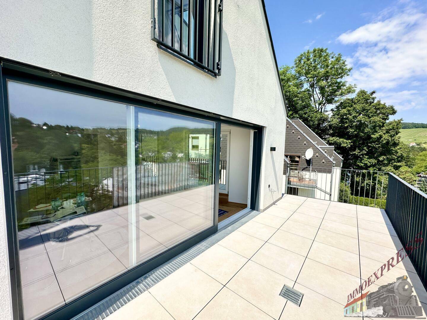 Breite Terrasse mit Schiebetür und Blick auf die grüne Umgebung.
