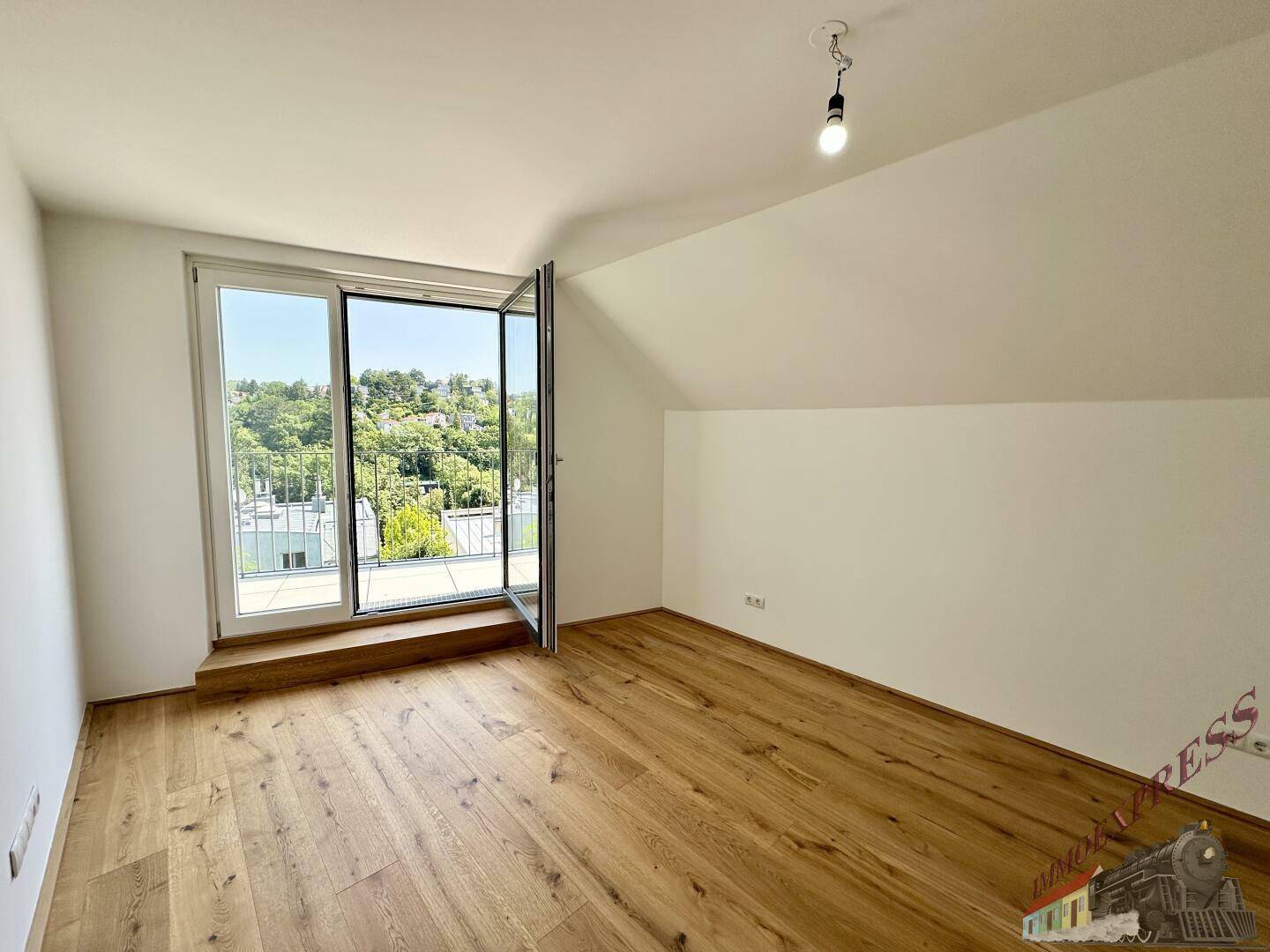 Dachgeschosszimmer mit Holzboden und großem Fenster mit Blick ins Grüne.