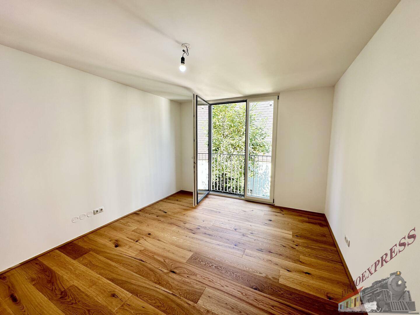 Geräumiges Zimmer mit Holzboden und Fenster zum grünen Außenbereich.