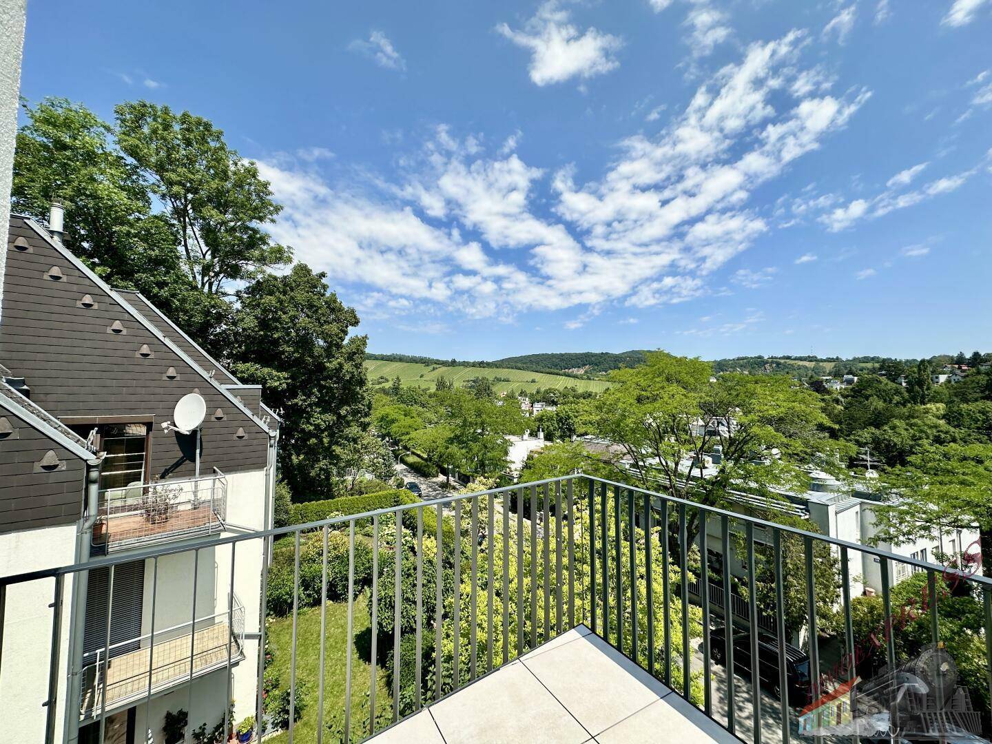 Sonniger Balkon mit Fliesenboden und Blick auf die umliegende grüne Hügellandschaft.