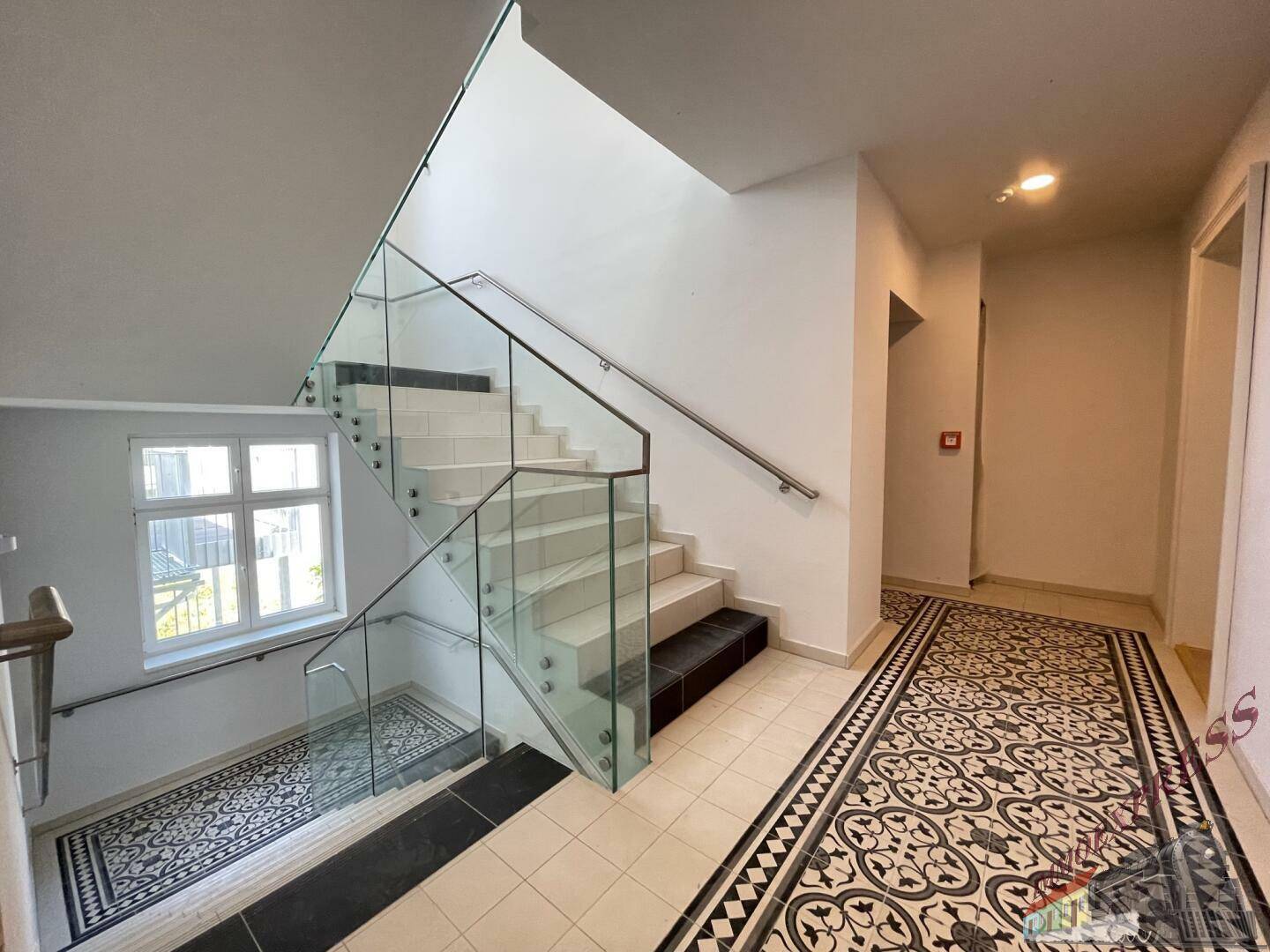 Helles Treppenhaus mit modernen Glasgeländern und dekorativem Fliesenboden.