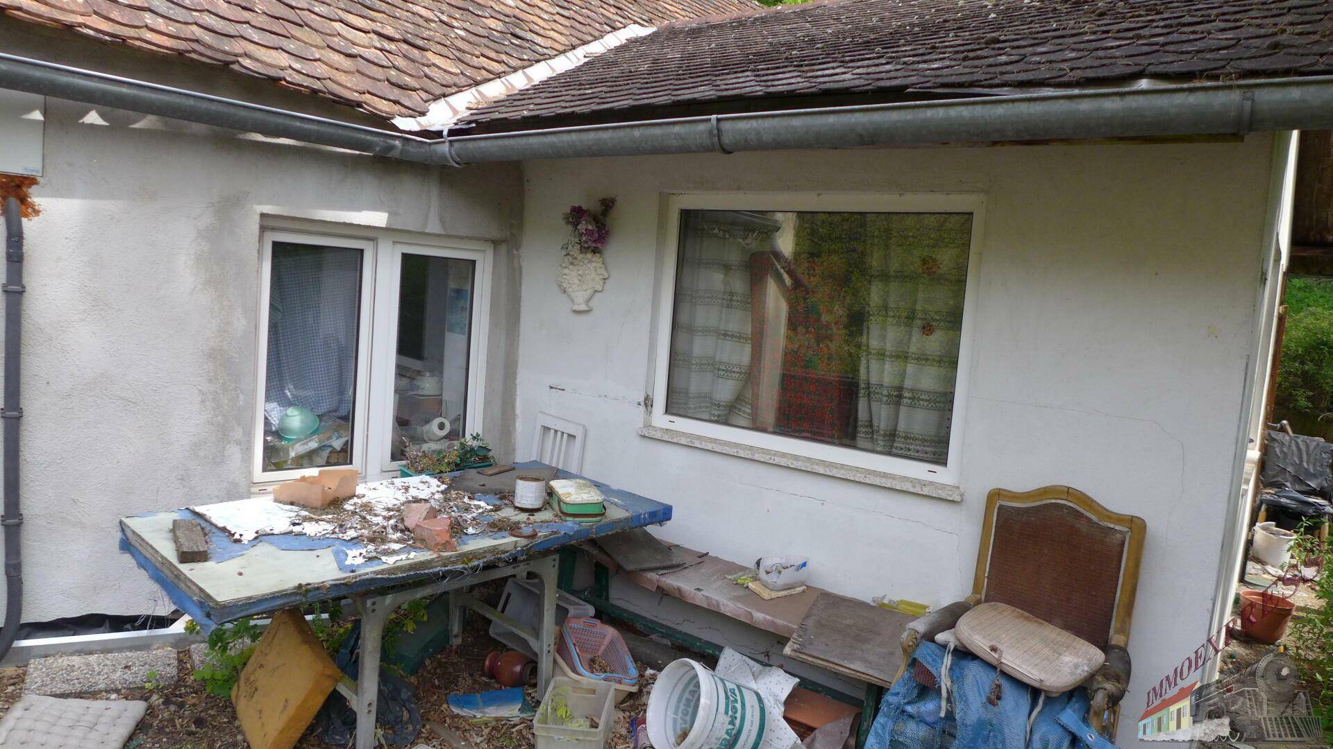 Detailansicht der Hauswand mit Fenstern und einem provisorischen, unaufgeräumten Außenbereich.
