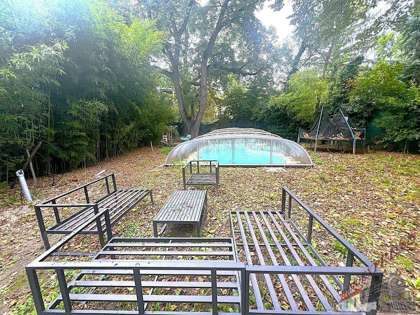 Großer Gartenbereich mit einem überdachten Pool, umgeben von Bäumen und Laub.