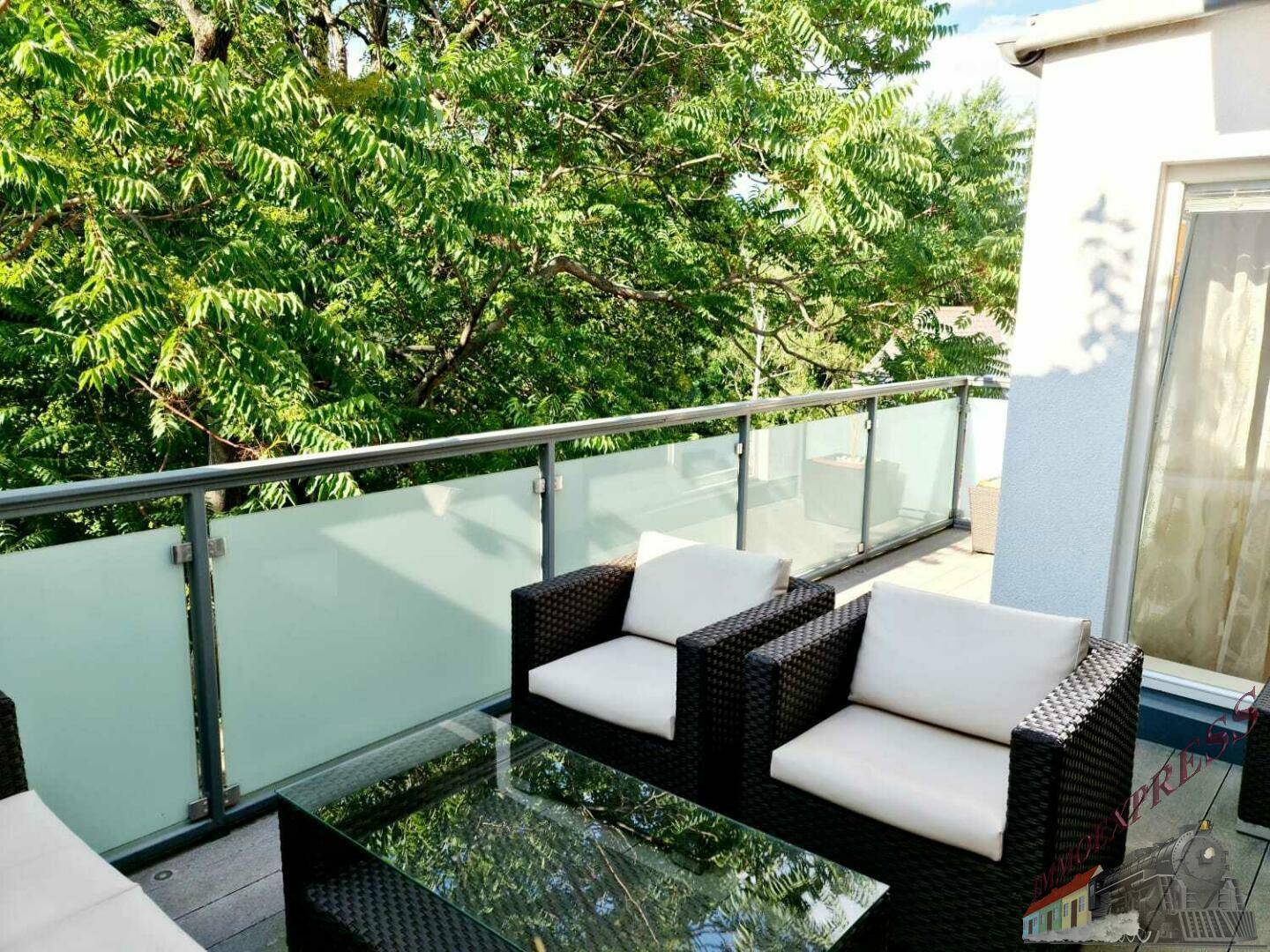 Gemütlicher Balkon mit Rattanmöbeln und einem Tisch, umgeben von dichtem Grün.