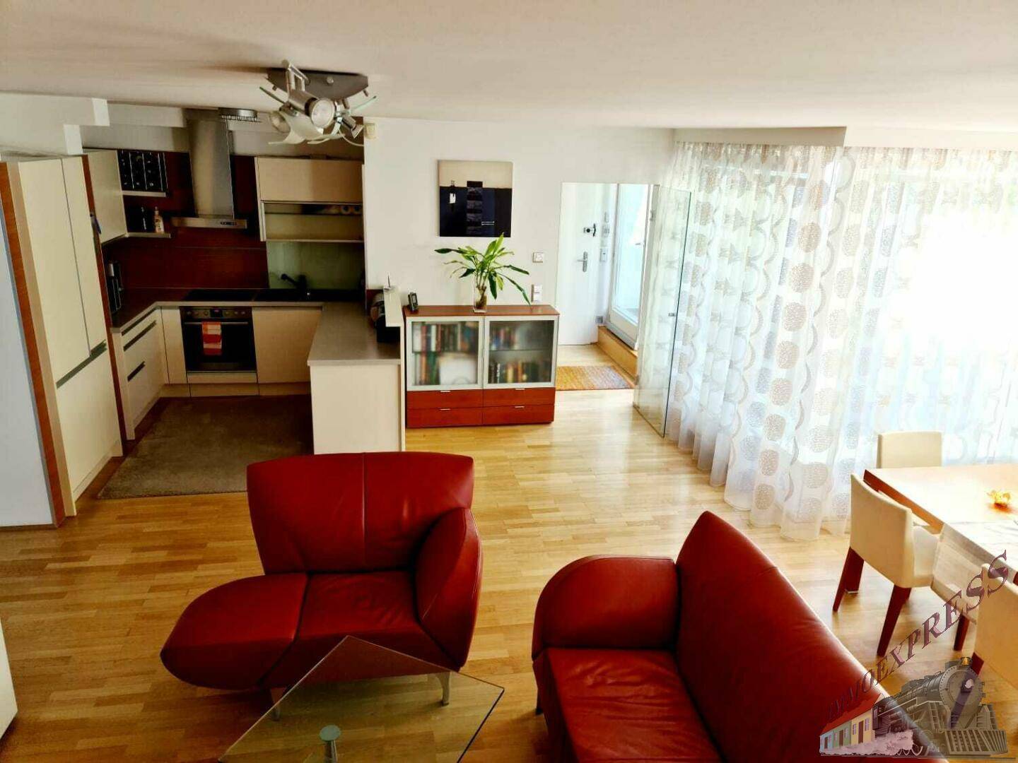 Heller offener Wohn-Essbereich mit integrierter Küche, Holzboden und Zugang zum Balkon.