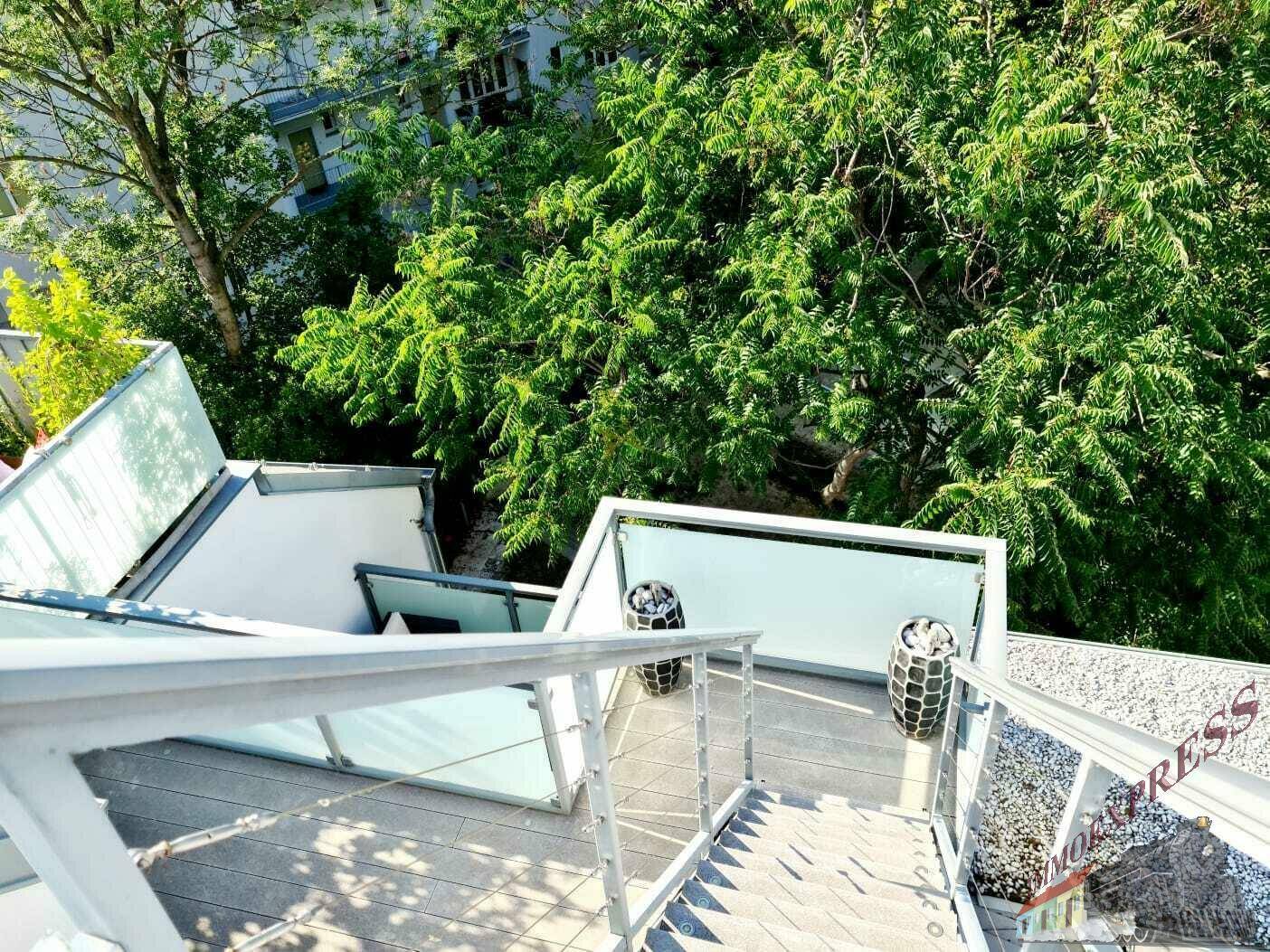 Außentreppe führt zu einer oberen Terrasse mit Blick auf üppiges Grün und Bäume.