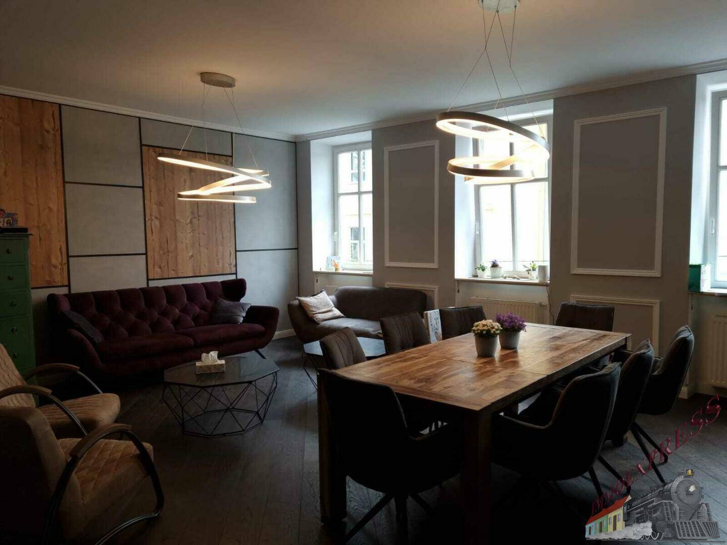 Stilvoller Wohn- und Essbereich mit Holzboden, modernen Leuchten und großen Fenstern.