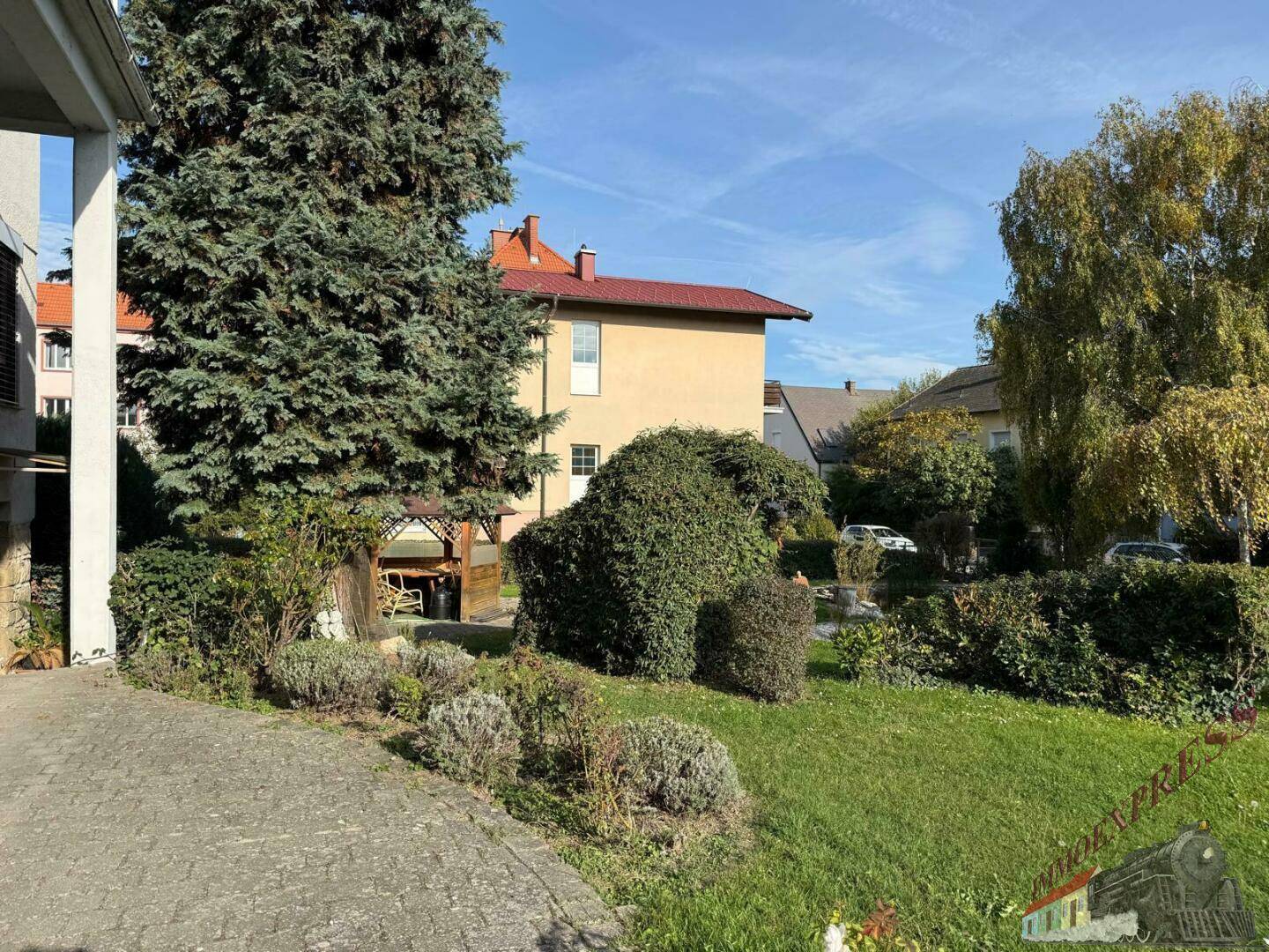 Seitlicher Gartenbereich mit Rasenfläche, Bäumen und einem gepflasterten Weg.