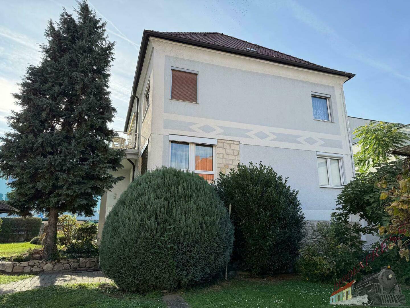 Seitenansicht des Hauses mit gepflegter Fassade, großen Fenstern und üppiger Bepflanzung.