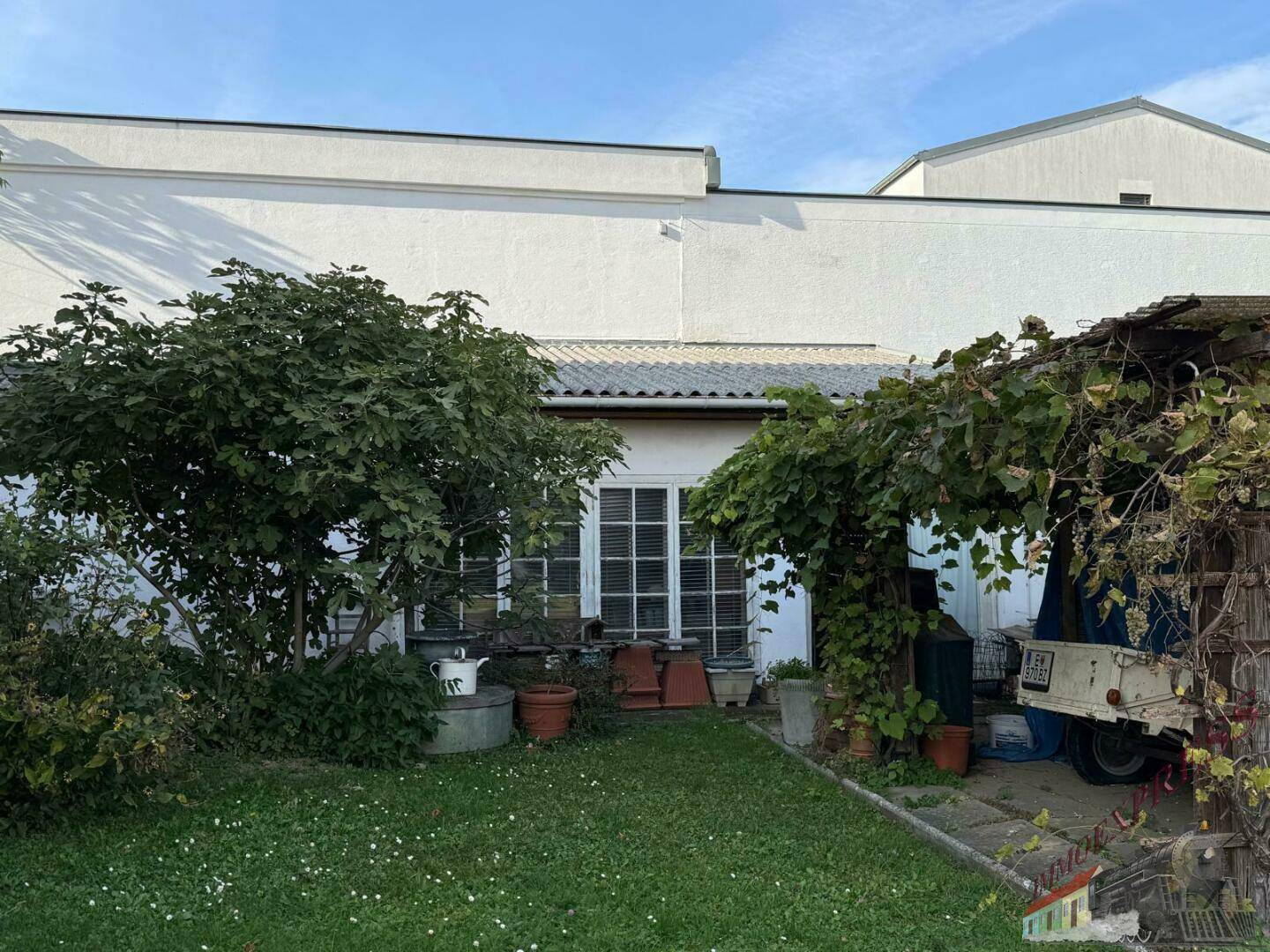 Hinterhofbereich mit üppiger Vegetation, Bäumen und einem überdachten Sitzbereich.