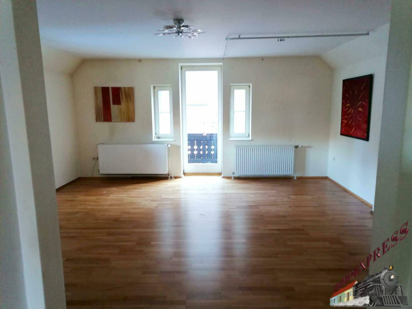 Heller Raum mit Laminatboden, Heizkörpern und Zugang zu einem französischen Balkon.