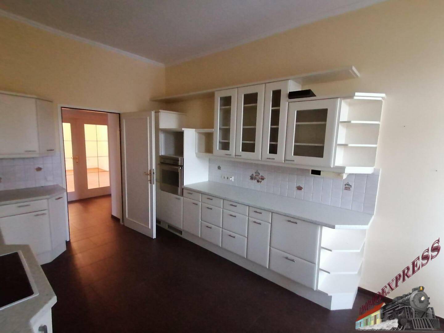 Helle Einbauküche mit weißen Schränken, integrierten Geräten und dunklem Boden.