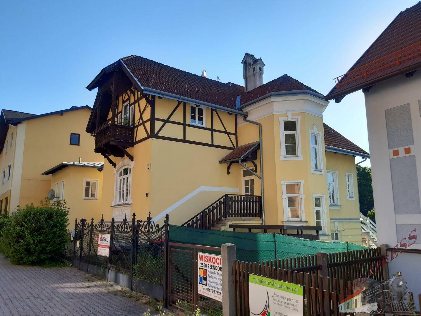 Gelbes Wohnhaus mit Fachwerkdetails und Balkon von der Straße aus gesehen.