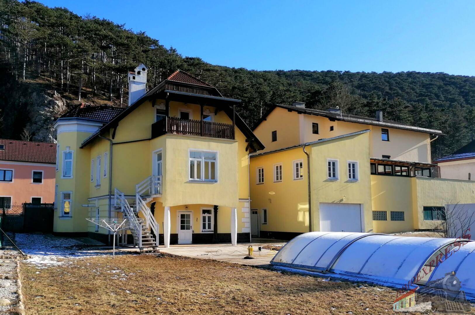 Ansicht des gelben Wohnhauses mit Balkon, Garage und Gartenbereich im Winter.