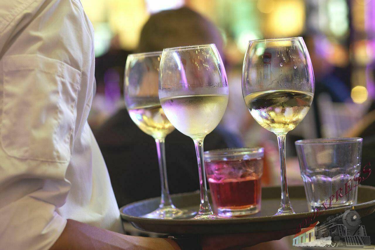 Ein Kellner serviert auf einem Tablett mehrere Gläser Wein und andere Getränke in einem Restaurant.