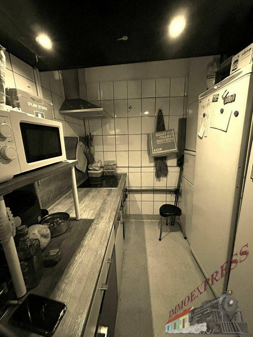 Eine kleine Küche mit Mikrowelle, Kühlschrank und gefliesten Wänden in einem funktionalen Stil.