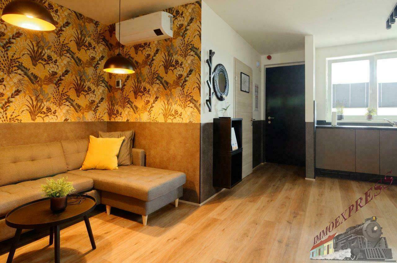 Gemütlicher Wohnbereich mit Sofa, dekorativer Tapete und Blick zur Küche und Eingang.