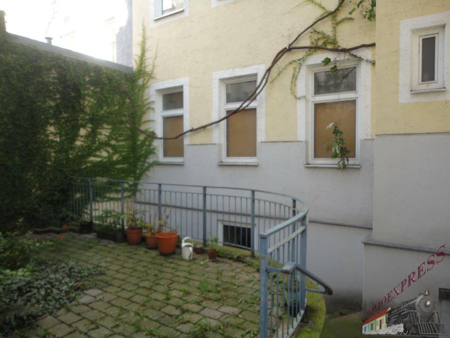 Begrünter Innenhof mit gepflastertem Bereich und einer Rampe, die zum Untergeschoss führt.